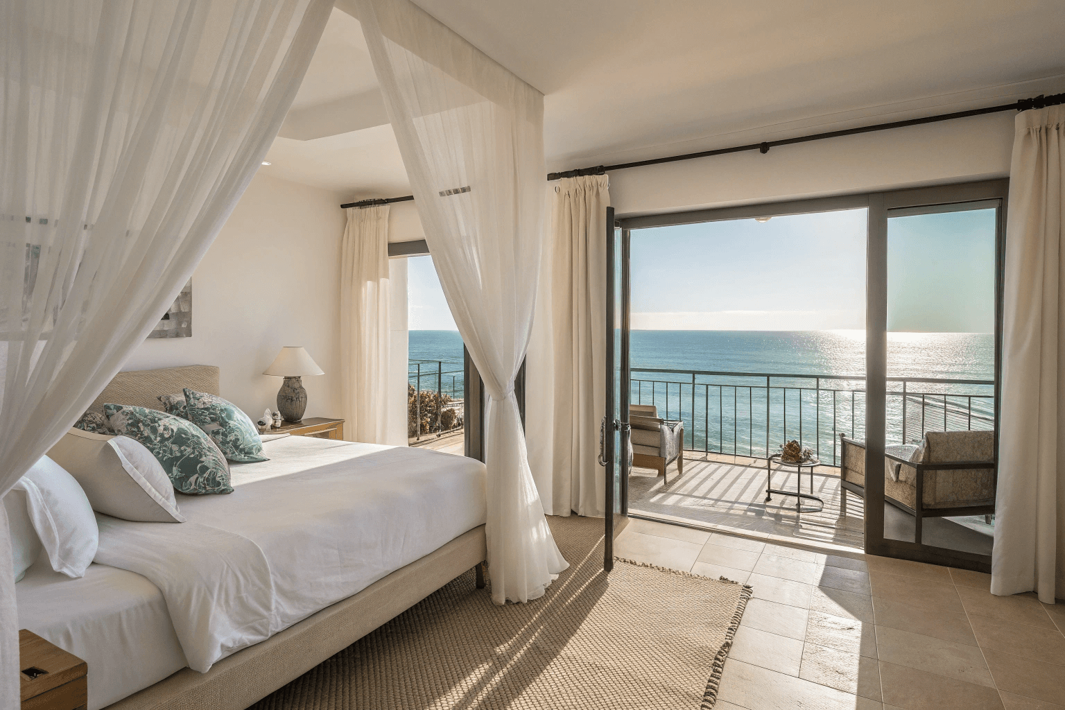 the entire room interior, ocean horizon visible, king bed neatly made, airy curtains flowing in the breeze.